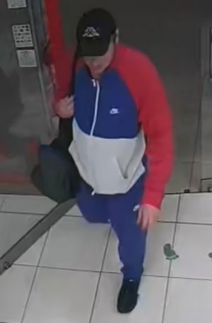 mężczyzna ubrany jest w dres w kolorze niebiesko-czerwono-0białym, sportowe buty i czapkę z daszkiem na głowie. na ramieniu ma przewieszoną sportową torbę.