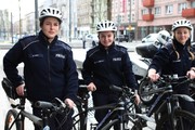 dwie policjantki w mundurach i kaskach stoją z rowerami policyjnymi na ulicy