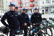 czterech policjantów w białych czapkach i mundurach stoi z rowerami na tle miasta