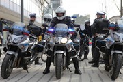 nie pierwszym planie policyjne motocykle, jeden z policjantów siedzi w kasku na środkowym motorze, w tle policjanci ruchu drogowego