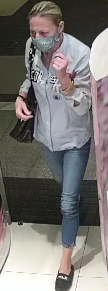 wizerunek kobiety podejrzewanej o kradzież kosmetyków. kobieta w wieku ok 40-50 lat, blond włosy spięte w kitkę, ubrana w jasną bluzkę, niebieskie spodnie, na ramieniu ma ciemną torbę oraz maseczkę na twarzy zasłaniającą nos i usta.