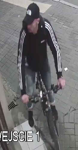 wizerunek mężczyzny podejrzewanego o kradzież z włamaniem. Mężczyzna ubrany jest w czarną bluzę z białymi paskami na ramionach, czarną czapkę z daszkiem i porusza się na rowerze.