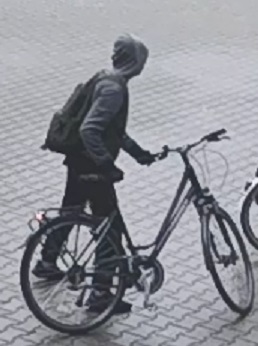 mężczyzna podejrzewany o kradzież roweru. mężczyzna szczupłej budowy ciała, ubrany w ciemnoszarą bluzę z kapturem na głowie, czarną maseczkę na twarzy, rękawiczki, czarne spodnie dresowe, białe skarpetki, czarne obuwie sportowe oraz ciemnozielony plecak