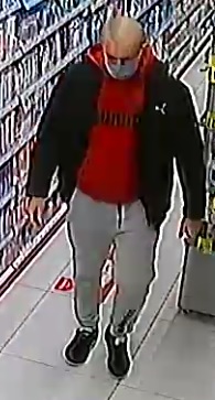 mężczyzna podejrzewany o kradzież perfum i szczoteczek elektrycznych. mężczyzna ma szare spodnie dresowe, czerwoną bluzę z kapturem, czarną kurtkę, czarne buty, jest łysy i ma maseczkę na twarzy zakrywającą nos i usta.