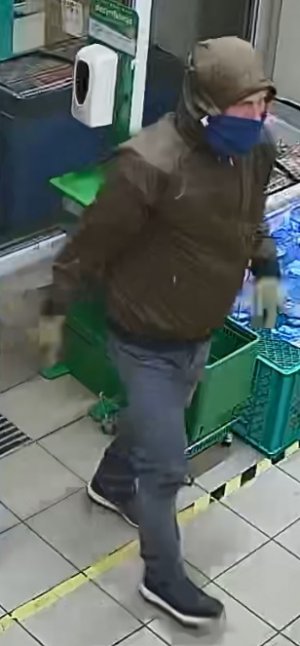 mężczyzna podejrzewany o kradzież puszki z zawartością pieniędzy, mężczyzna ma zielona kurtkę z kapturem na głowie, maseczkę na twarzy zasłaniającą nos i usta, spodnie typu dżinsy i sportowe buty .