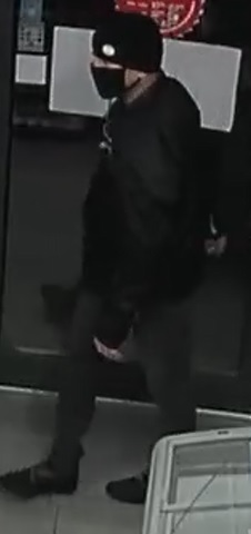 mężczyzna ubrany w czarną czapkę z białym elementem, czarną kurtkę sportową, ciemne spodnie, sportowe czarne buty i czarną maseczkę zasłaniającą usta i nos.