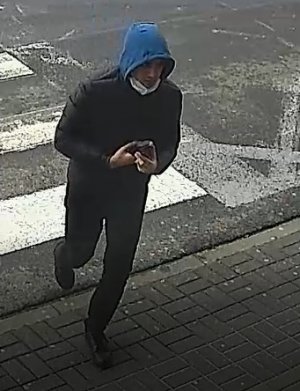mężczyzna w wieku około 30-35 lat, ubrany w ciemną pikowaną kurtkę, ciemne spodnie, ciemne obuwie, na głowie ma niebieski kaptur, jest szczupłej budowy ciała
