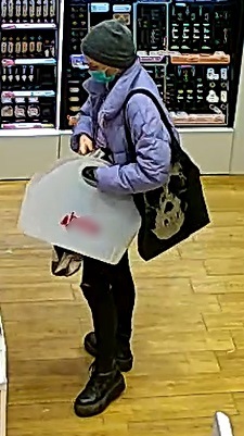 kobieta ubrana w zimową, fioletową kurtkę, zimową czapkę, czarne spodnie, ciemne buty, w ręku trzyma torbę i torebkę, ma blond włosy, jest szczupłej budowy ciała