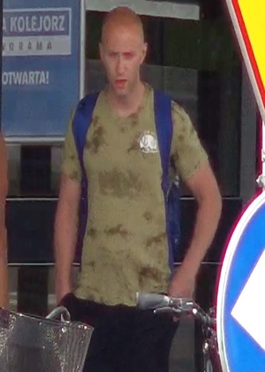 mężczyzna wysoki, szczupły, około 35-40 lat, ubrany w koszulkę tshirt z krótkim rękawem oraz dresowe krótkie spodnie, na plecach ma założony niebieski plecak