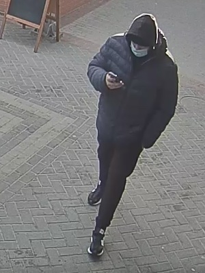 mężczyzna w wieku ok. 25 lat, ubrany w granatową kurtkę - pikowaną, ciemne spodnie, ciemne buty z białymi wstawkami, na głowie miał kaptur,  a na twarzy białą maseczkę zasłaniającą usta i nos