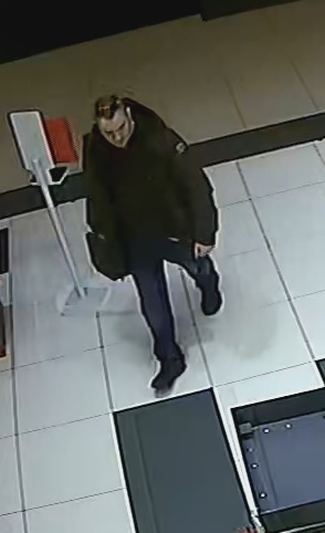 mężczyzna wieku około 40-45 lat, ubrany w ciemne dżinsy, sportowe ciemne buty, ciemną kurtkę, ma zawieszoną torbę na prawe ramię, a na głowie ma założone okulary